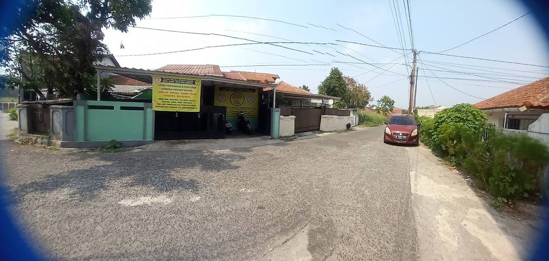 Jalan menuju Rumah Terapi Elektrostatik Dr. JISM di Ciomas, dengan rumah berpagar hijau di tepi jalan.
