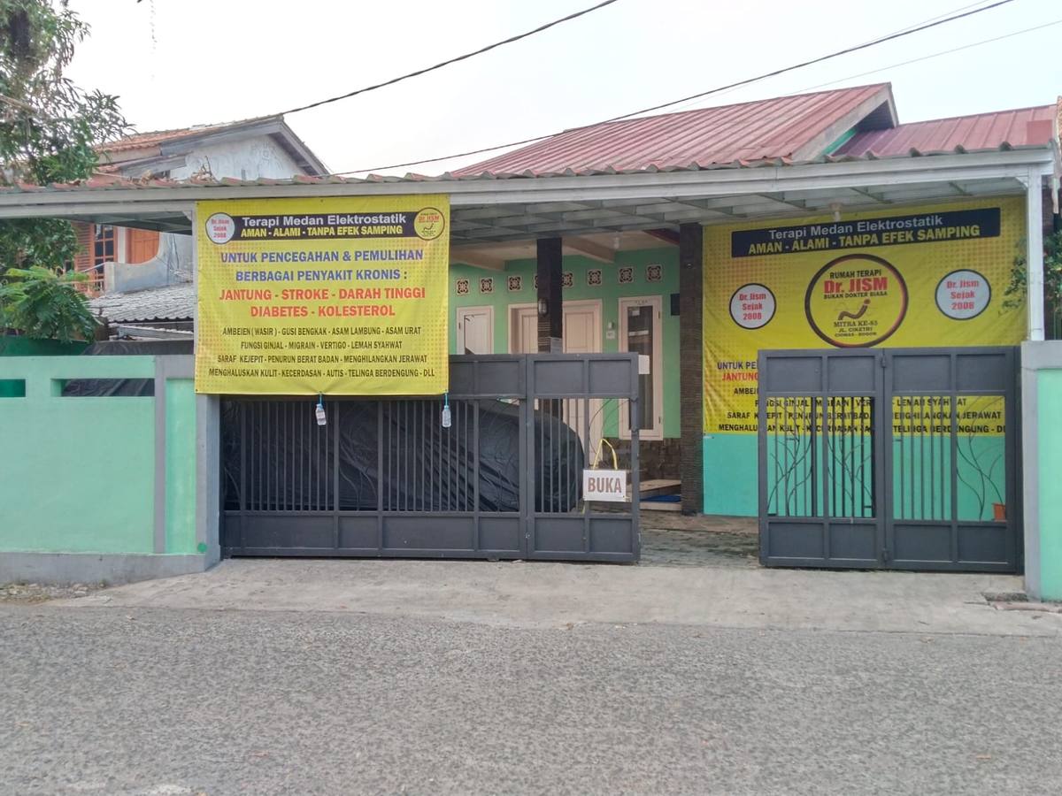 Tampak depan Rumah Terapi Elektrostatik Dr. JISM di Jalan Cikerti, Ciomas: rumah berpagar hijau, atap merah, dan gerbang besi.